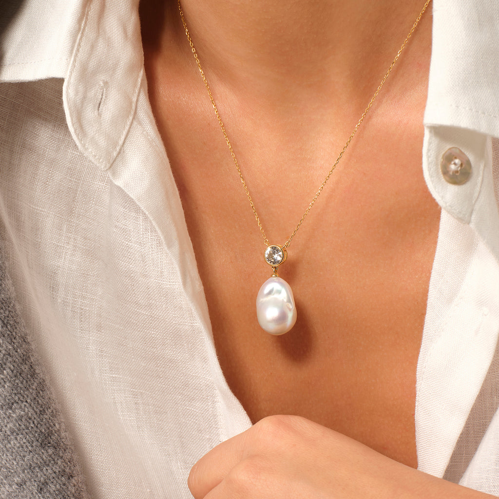 Model wearing baroque freshwater pearl and round cubic zirconia pendant necklace in yellow gold color