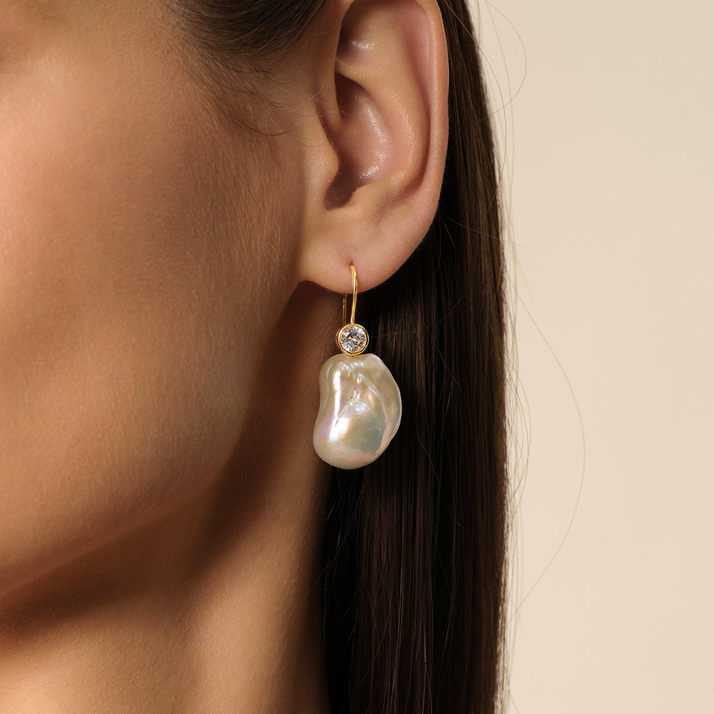 Close-up of model wearing baroque freshwater pearl and round cubic zirconia hook earrings in yellow gold color