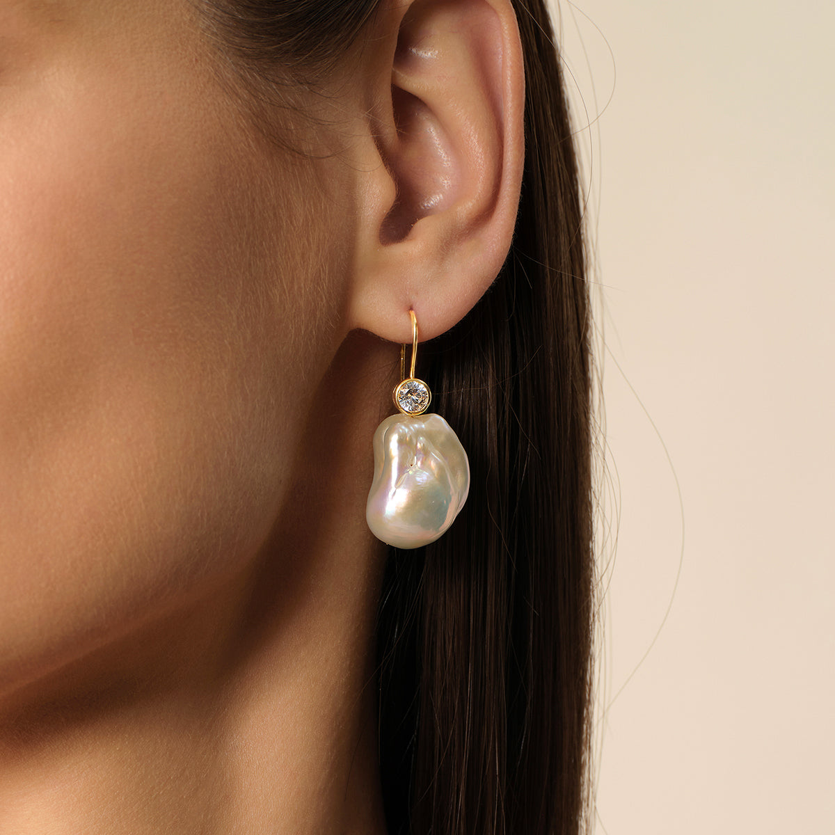 Close-up of model wearing baroque freshwater pearl and round cubic zirconia hook earrings in yellow gold color