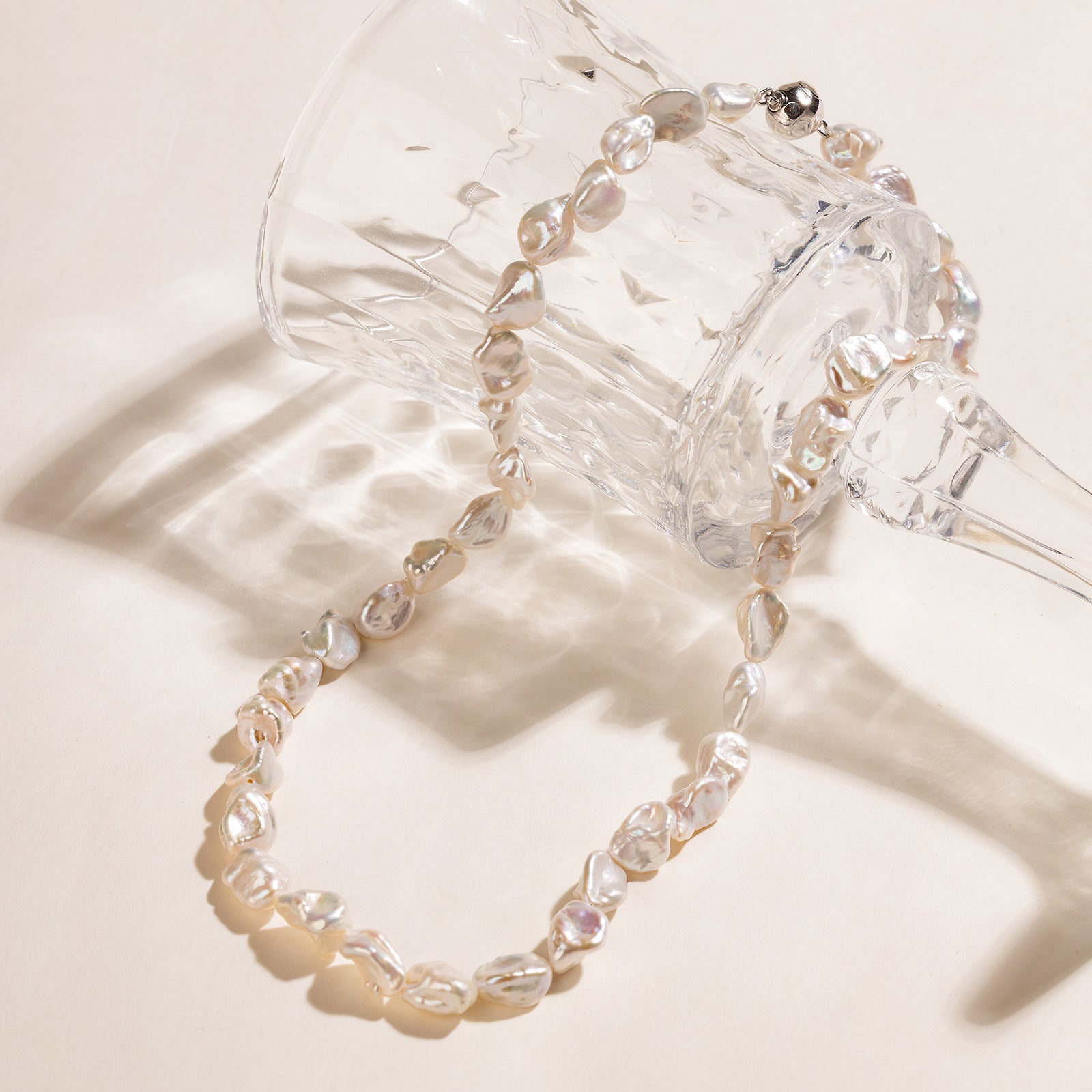 Iridescent freshwater Keshi pearl strand necklace shown on clear glass