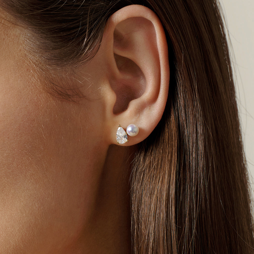 Close-up of model wearing freshwater pearl and pear-shaped cubic zirconia stud earrings in yellow gold color