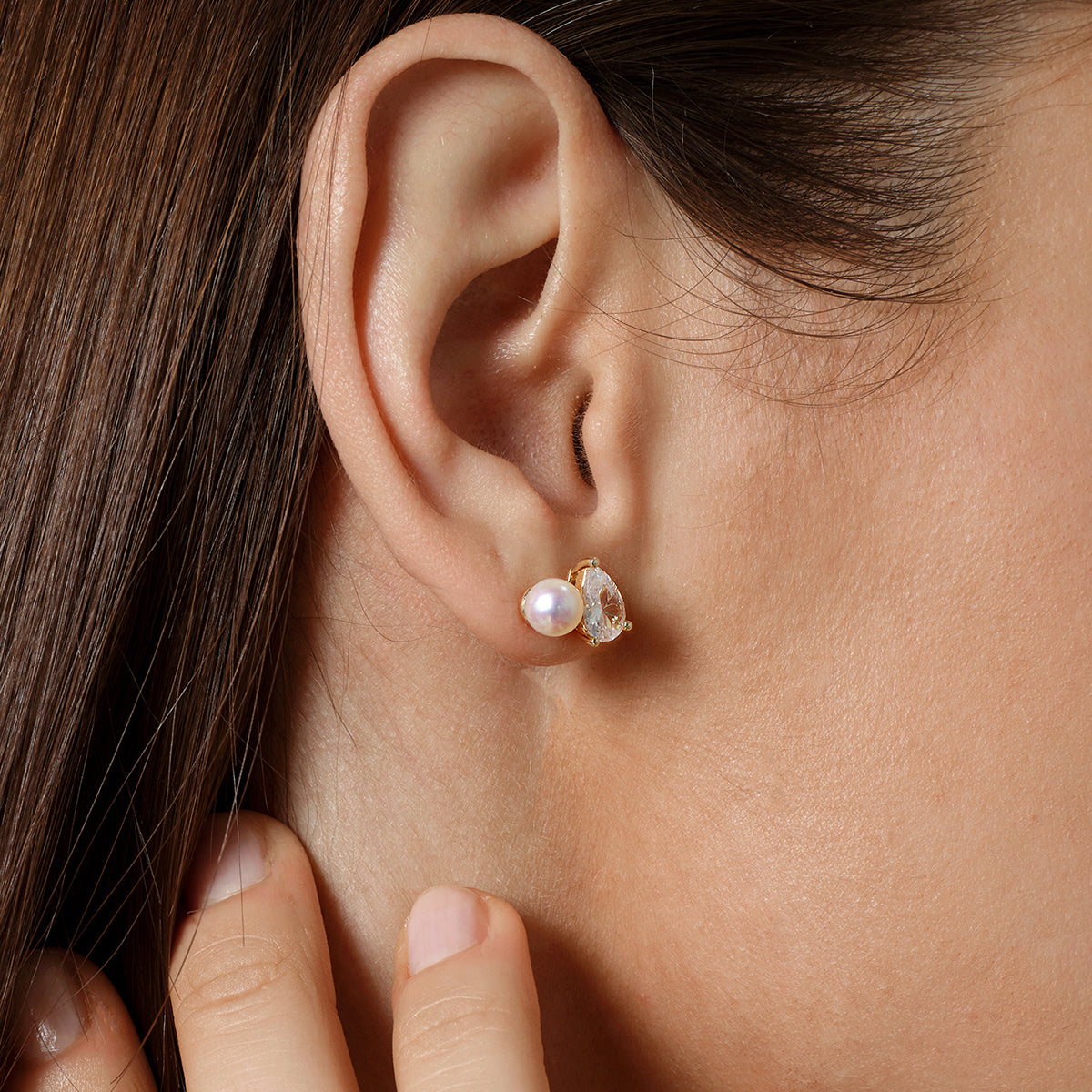 Model wearing freshwater pearl and pear-shaped cubic zirconia stud earrings in yellow gold color with neutral styling