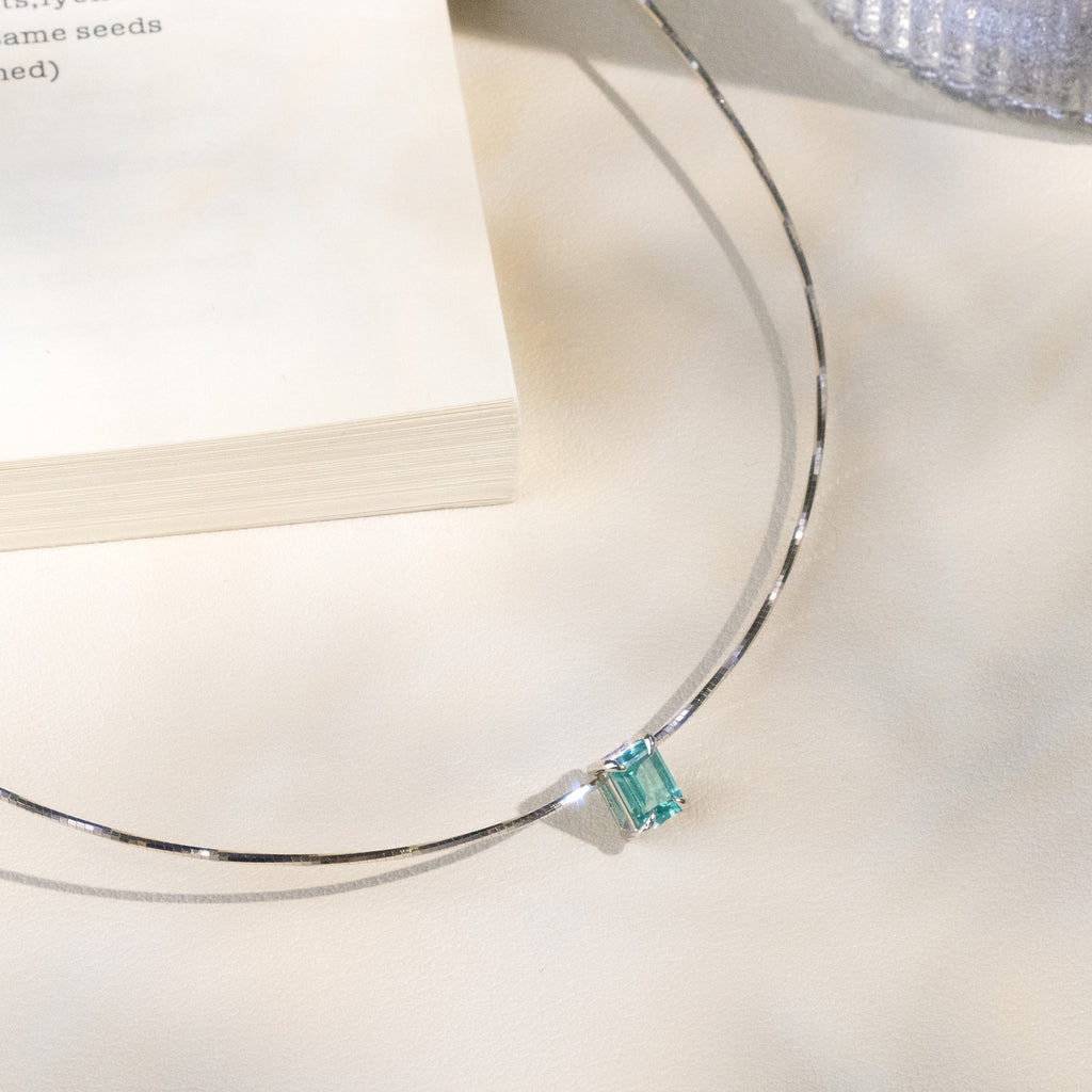 Close-up of a blue-green rectangular lab-created Paraiba garnet pendant on a silver chain