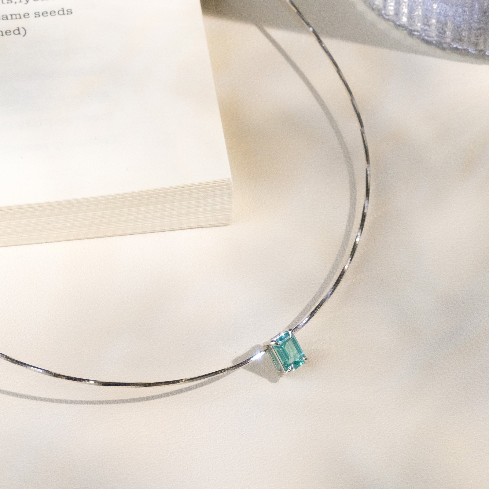 Close-up of a blue-green rectangular lab-created Paraiba garnet pendant on a silver chain