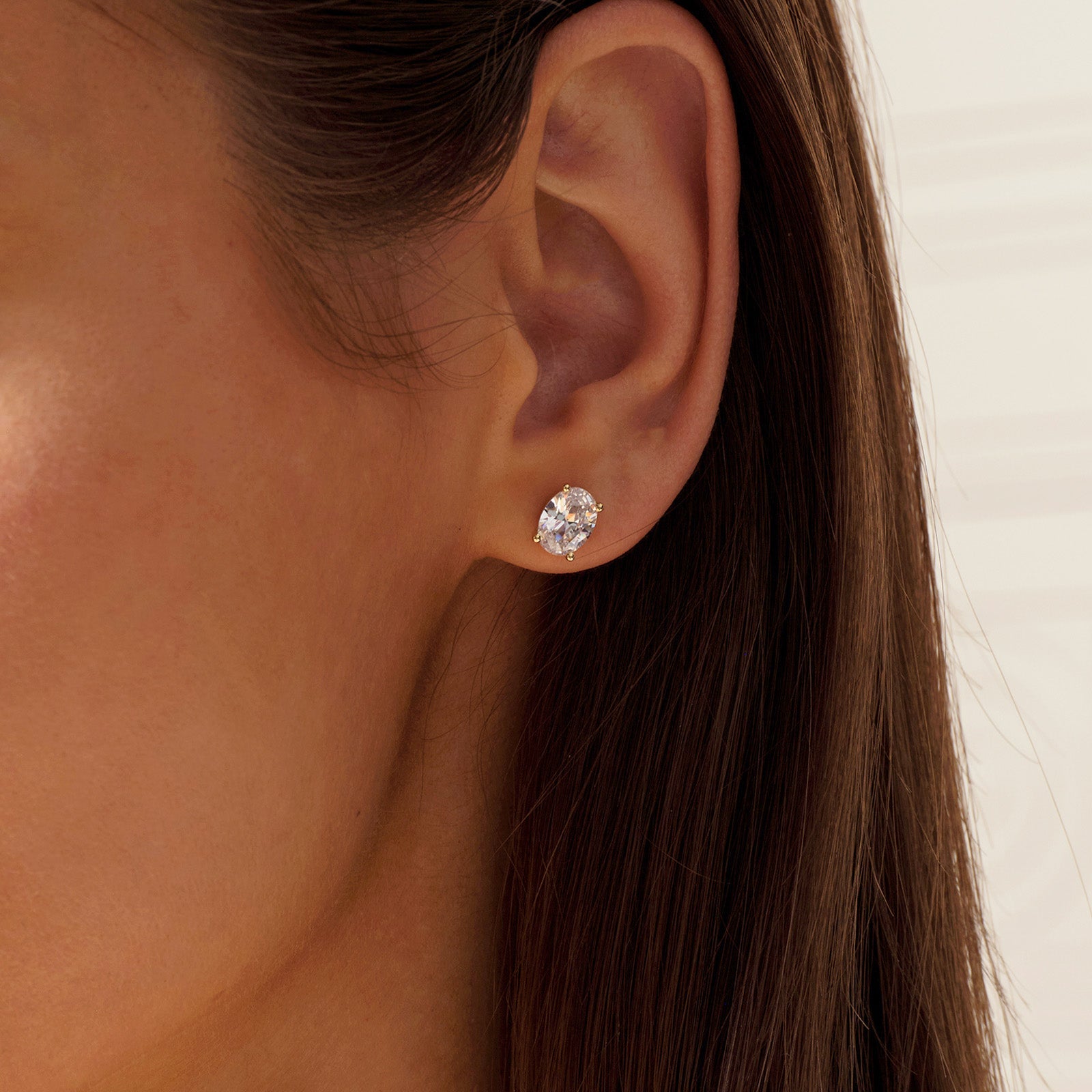Close-up of model wearing oval cubic zirconia stud earrings in gold color
