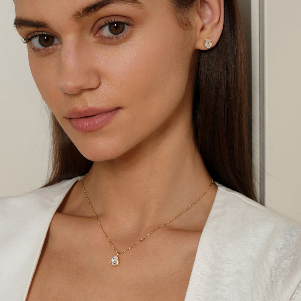 Model wearing pear-shaped cubic zirconia pendant necklace in yellow gold color with neutral outfit