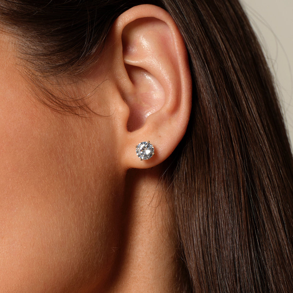 Model wearing round cubic zirconia stud earrings in gold color angle view