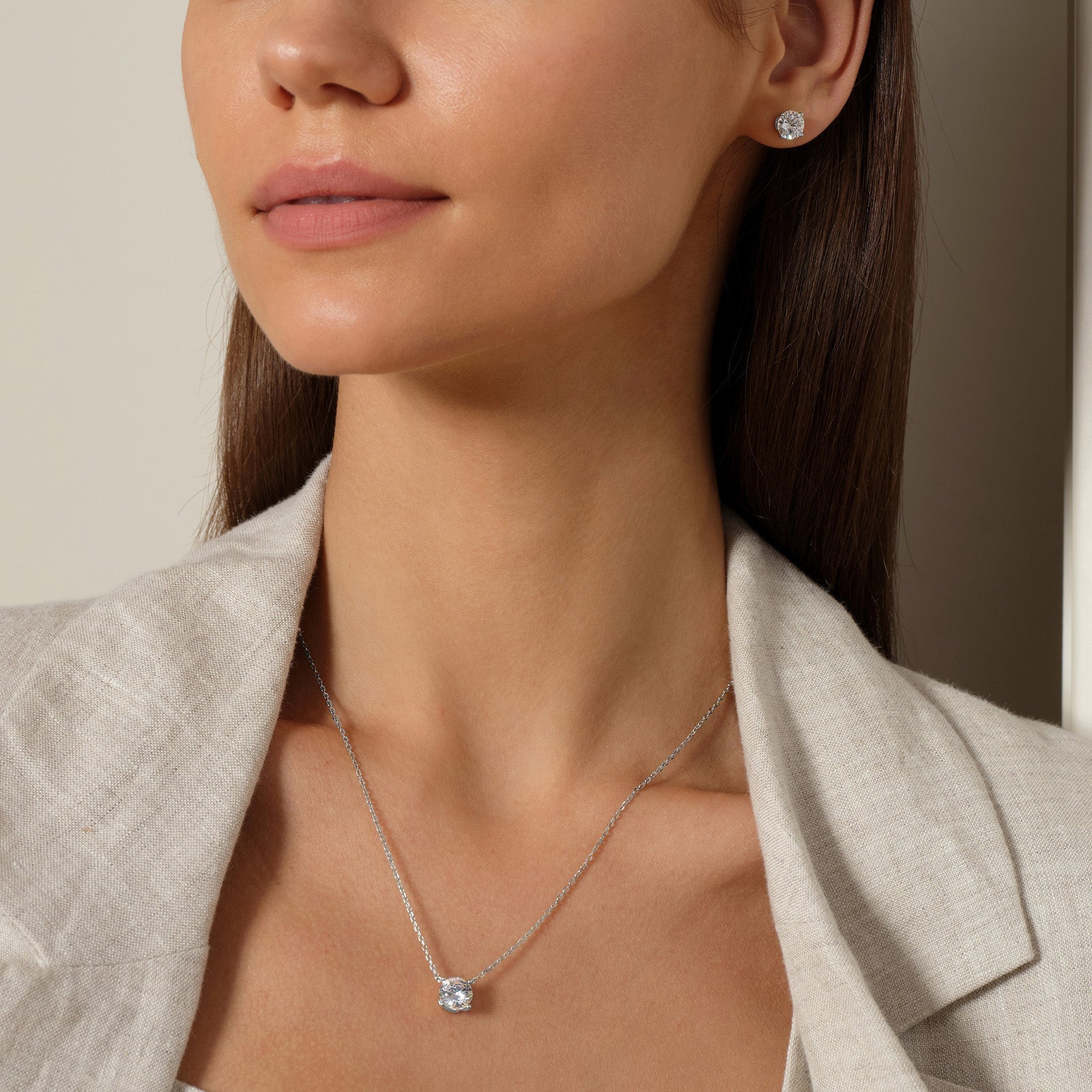 Model wearing round cubic zirconia stud earrings in silver color with neutral outfit